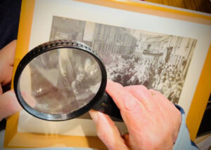 John looks at a black and white photograph of Gwydir Street residents celebrating VE Day through a magnifying glass.